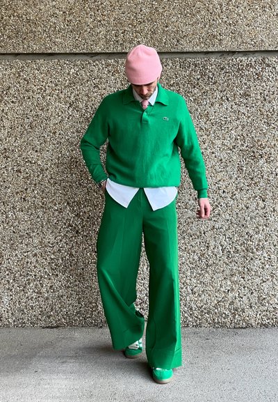 Polo de forro verde con cuello blanco, combinado con pantalones anchos verdes y zapatillas verdes. Lleva puesto un gorro ligero de color rosa.