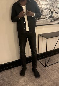 Czarna kurtka dżinsowa z kołnierzem, biały sweter i czarne spodnie o dopasowanym kroju. Gładka tekstura, minimalne detale, brak widocznych wzorów.