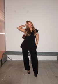 Svart skräddarsydd jumpsuit med korta ärmar, avsmalnande ben och en subtil peplummidja; kombineras med spetsiga klackar och en liten handväska.