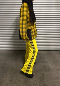 Oversized yellow plaid jacket with black accents, teamed with high-waisted yellow trousers that have three black stripes running down the sides.