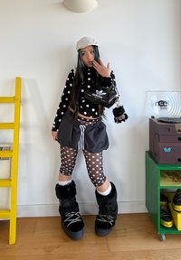 Mustavalkoinen pilkullinen pitkähihainen paita, läpikuultavat pilkulliset leggingsit, ylisuurikokoinen harmaa hame ja mustat turkiksella vuoratut saappaat. Asusteena pieni musta laukku.