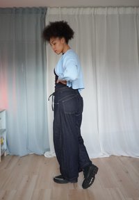 Denim wijde broek met een hoge taille en achterzakken. Gecombineerd met een lichtblauwe cropped cardigan en zwarte schoenen. Soepele textuur.