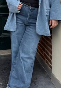 Hellblaue Denim-Hosen mit weitem Bein und hohem Bund, kombiniert mit einem passenden übergroßen Blazer, der eine weiche Textur und minimale Details zeigt.