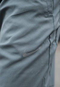 Shorts de sport en tissu gris foncé avec un logo Nike subtil sur le côté, montrant la texture du tissu et les détails des coutures.
