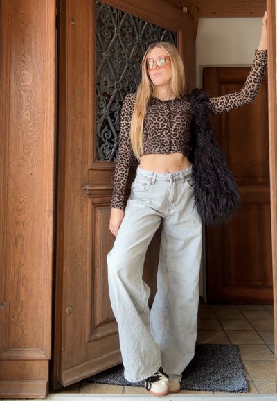 Top corto de estampado de leopardo, jeans de pierna ancha en gris claro y bolso negro de pelo. El calzado presenta una suela clara con cordones oscuros.