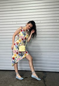 Blumendruckkleid in Pink, Gelb und Blau mit bindbaren Trägern; kombiniert mit hellblauen Ballerinas und einer kleinen runden gelben Umhängetasche.