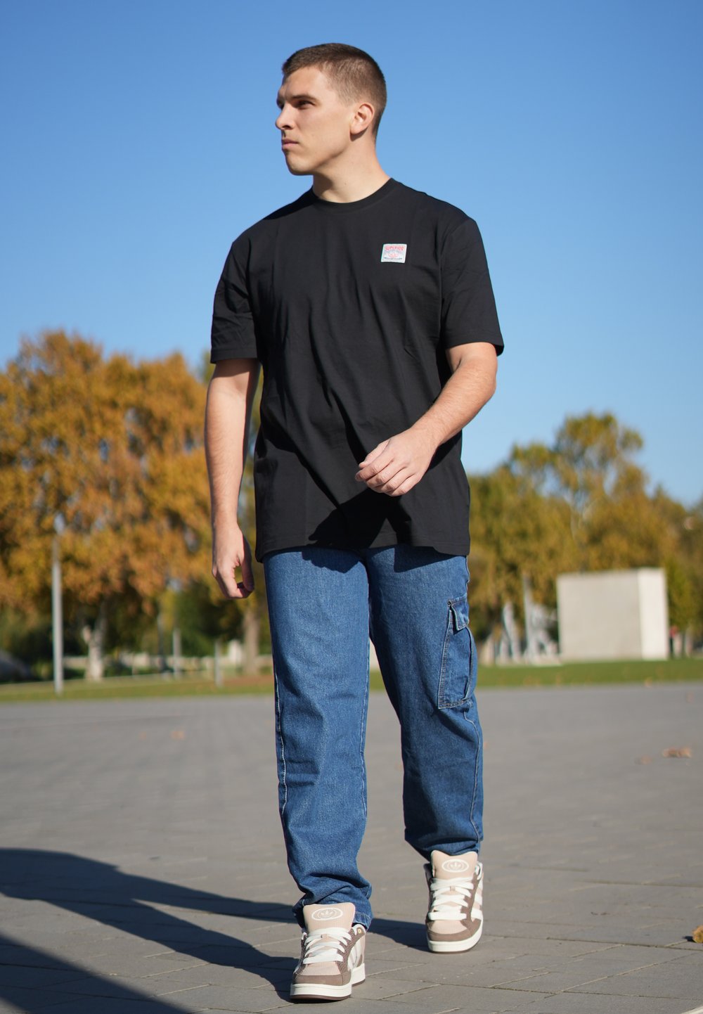 Sort bomulds T-shirt med korte ærmer og et logo-patch, parret med blå cargo-jeans med sidelommer og lyse sko.