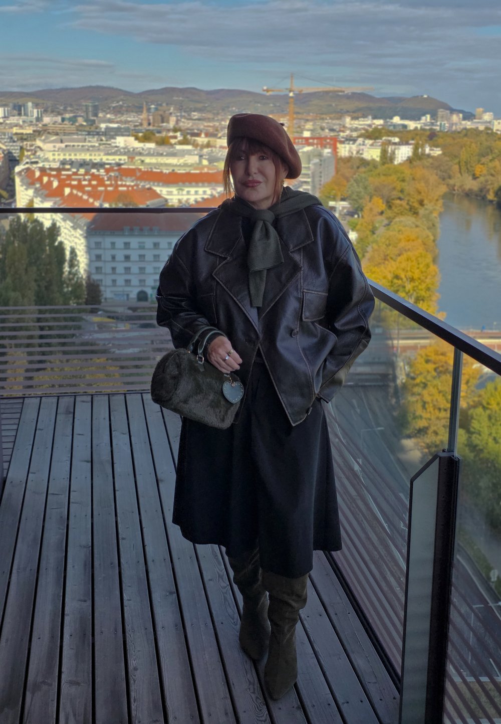 Smeđa kožna jakna s zelenim šalom, crna haljina i smeđe čizmice do koljena. Drži okruglu, sivu tašnu s privjeskom u obliku srca.