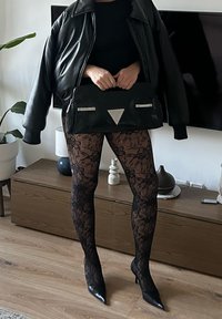 Juoda odinė bombonešio stiliaus striukė ant aptemptos palaidinės, derinama su juodomis nėriniuotomis pėdkelnėmis ir smailiais juodais aukštakulniais. Laiko juodą rankinę su sidabro akcentais.