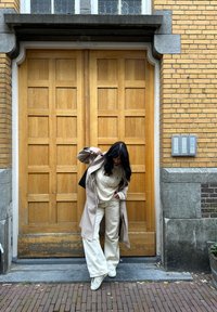 Hele beeži trench-coat kreemja sviitriga ja avarate pükstega, koos valgete tossudega. Puidust paneelidega sissepääs, millel on tekstuuriga kivielemendid.