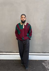 Μαρόν και πράσινο διακοσμημένο πλεκτό πουλόβερ με μπεζ γιακά, συνδυασμένο με μαύρα φαρδιά παντελόνια και μαύρα παπούτσια. Γκρίζο φόντο.