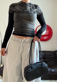 Haut noir à manches courtes avec une texture en denim usée, associé à un pantalon de survêtement gris. Tient un petit sac en cuir noir avec double sangle.