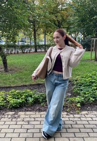 Svetlo béžový cardigan s gombíkmi, tmavofialový top, voľné svetlo modré džínsy, čierne tenisky, nesúci béžovú tašku s patterned šálom.