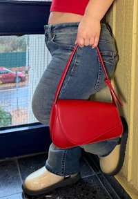 Sac à main en cuir rouge avec une forme arrondie et des détails de couture remarquables. Fermeture à rabat incurvé et une seule bandoulière.