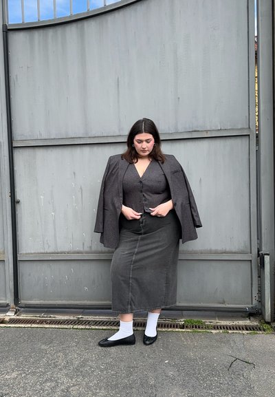 Blazer gris a medida combinado con una blusa de botones gris a juego y una falda de mezclilla larga. Bailarinas negras y calcetines blancos completan el atuendo.