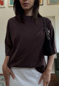 Maglietta marrone a maniche corte con una vestibilità comoda, abbinata a una gonna bianca. Una piccola borsa nera con tracolla intrecciata completa il look.