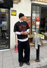 T-shirt graphique noire avec texte rouge sur une chemise blanche à col, associée à un pantalon noir ample et des baskets noires. Accessoires comprennent une chaîne.