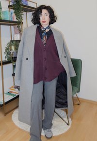 Sivý dlhý kabát cez burgundskú vestu so zapínaním na gombíky a sivé nohavice, doplnené námorníckym vzorovaným šálom a sivými topánkami; textúrovaná látka, voľný strih.