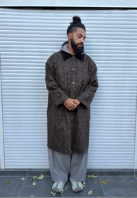 Manteau à imprimé léopard avec une base marron foncé, col en velours côtelé marron, associé à un pantalon ample gris et des baskets grises. Tissu texturé visible.