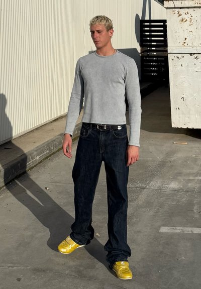 Camisa de manga larga acanalada gris, pantalones vaqueros oscuros y zapatos amarillos brillantes. Textura suave con un corte ajustado y un diseño simple.