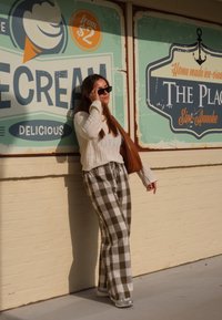 Ανοιχτό μπεζ πλεκτό πουλόβερ, καφέ και λευκό καρώ παντελόνι, γκρι αθλητικά παπούτσια και καφέ τσάντα. Το φόντο διαθέτει πολύχρωμα επιγραφικά στοιχεία εμπνευσμένα από παγωτό.