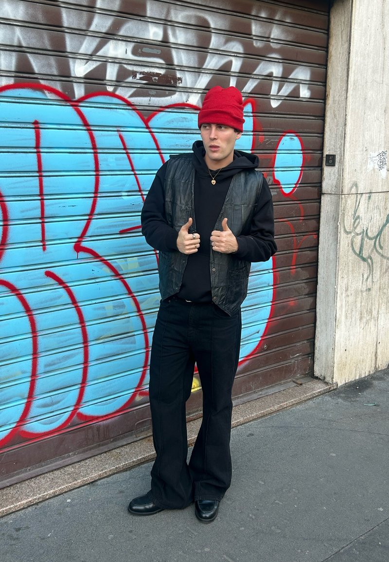 Sort lædervest over en sort hoodie, løse sorte bukser og skinnende sorte sko. En rød strikket hue og sølvringe fuldender looket.