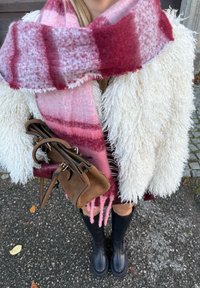 Hvid jakke i kunstpels, pink og rødternet tørklæde, brun ruskindstaske med sorte læderdetaljer, knæhøje sorte støvler og bare ben.