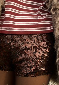 Haut à manches longues à rayures bordeaux et blanches, associé à un short pailleté noir et or rose, avec une finition lisse et texturée.