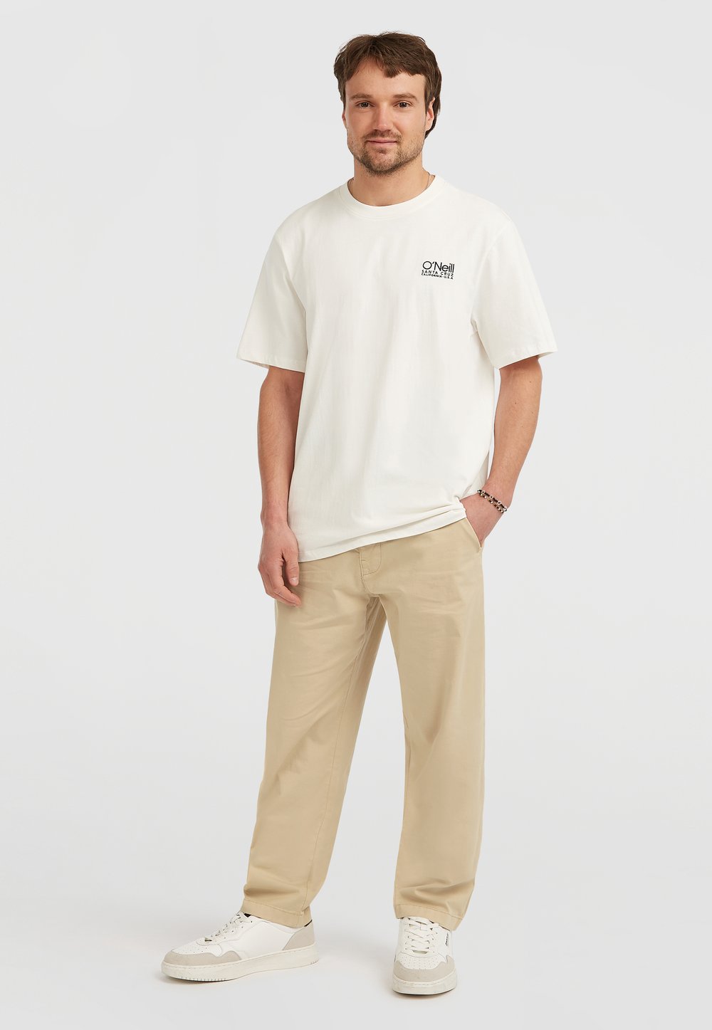 Licht beige oversized t-shirt met korte mouwen, voorzien van zwarte logo-print. Gecombineerd met licht kaki broek en witte sneakers.