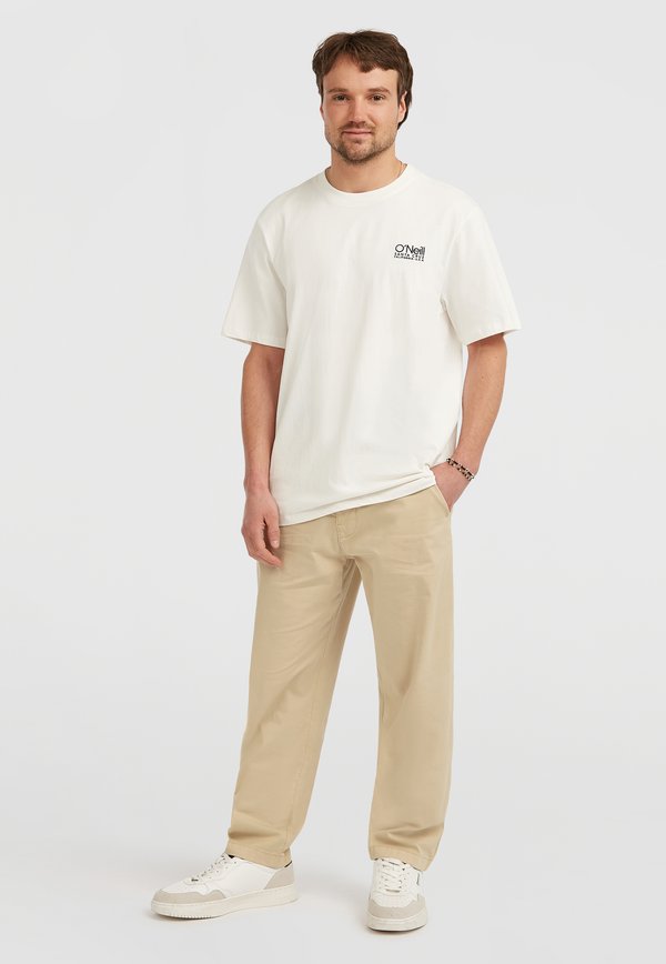 Licht beige oversized t-shirt met korte mouwen, voorzien van zwarte logo-print. Gecombineerd met licht kaki broek en witte sneakers.