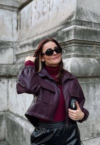 Κοντό σακάκι σε μπορντό χρώμα από τεχνητό δέρμα με δύο μπροστινές τσέπες, συνδυασμένο με ριγέ μπορντό φούτερ με ψηλό λαιμό και μαύρο παντελόνι με ελαστική μέση.