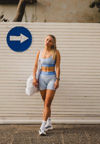 Conjunto atlético azul claro, incluindo um top cropped ajustado e calções de cintura alta, combinado com uma mala tote branca e ténis em preto e branco.