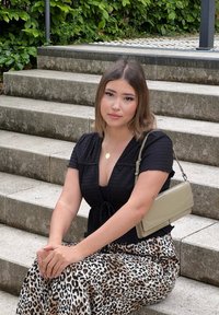 Blusa nera con texture e maniche corte, abbinata a una gonna con stampa leopardata. Una borsa beige pende dalla spalla, appoggiata su gradini in cemento.