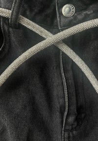 Črn denim material s križanimi srebrnimi kamenčki. Na vrhu pasu je viden kovinski gumb.