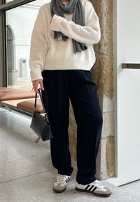 Hvid fluffy sweater, grå tørklæde, navy løse bukser, sort håndtaske og grå-hvide Adidas sneakers. Teksturomslag og afslappet pasform.