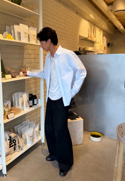 Hombre con camisa blanca y pantalones negros navegando por productos envasados en estantes blancos en el interior de una tienda moderna y con decoración minimalista.