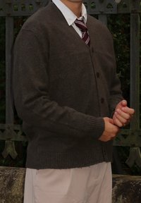 Brauner Wollcardigan mit V-Ausschnitt, Knopfleiste, gerippten Bündchen und Saum. Über einem weißen Hemd und einer kastanienbraunen Krawatte getragen, mit einer strukturierten Oberfläche.