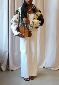 Fleece jacket with cow print, white tank top, high-waisted white flared jeans, brown suede handbag, and open-toe sandals.