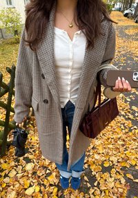 Brun houndstooth oversized frakke, hvid skjorte, blå jeans, mørkeblå sko, marmorfarvet håndtaske, sort paraply, faldende gule blade.