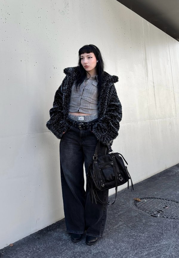 Faux fur black coat, cropped checked shirt, wide-leg black jeans, black belt, and a black handbag with fringe details. Flat shoes.