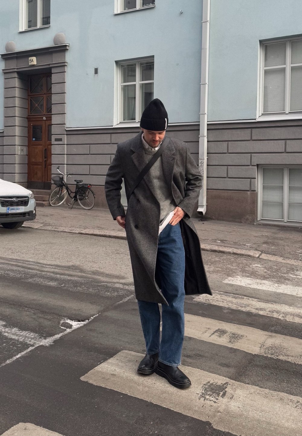 Szürke gyapjú keverék kabát, texturált kötött szürke pulóver, kék farmer, és fekete cipők, egy fekete sapkával kiegészítve. Városi jelenet zebrával.