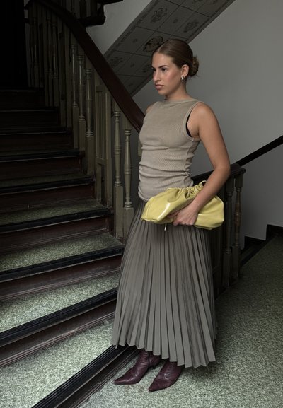 Top sin mangas beige combinado con una larga falda plisada verde oliva. El accesorio incluye un bolso amarillo con fruncido y botas burgundy de tacón.