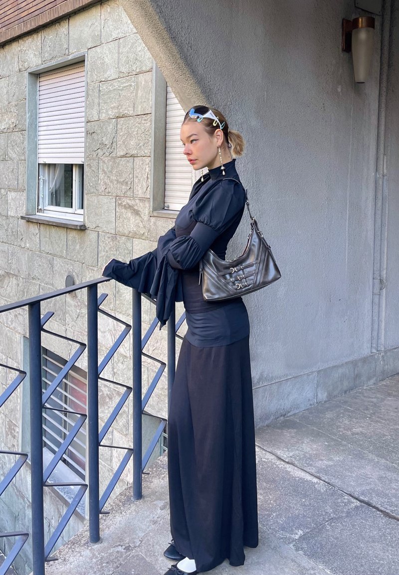 Μαύρο τοπ με μακριά μανίκια και φουσκωτά μανίκια, εφαρμοστή μέση και ρέουσα φούστα. Τα αξεσουάρ περιλαμβάνουν μια μαύρη τσάντα ώμου και ένα κλιπ για τα μαλλιά.