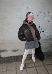 Hnedá kožená bomber bunda, šedá plisovaná sukňa, svetloružové tenisky a ružová čiapka s čiernobielym vzorovaným doplnkom. Štruktúrované látky.