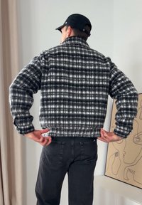 Casaco às riscas preto e branco com design curto, tecido texturizado e punhos canelados, combinado com calças pretas e um boné.