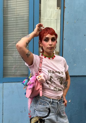 Bolso de cuero rosa con llaveros de peluche, pantalones cortos de mezclilla gris con un diseño de gato y una camiseta gráfica rosa clara con un estampado brillante.