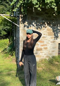 Camiseta negra de manga larga combinada con pantalones sueltos de color gris oscuro, con cintura elástica. Una gorra verde con logotipo completa el conjunto.
