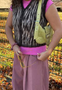 Veste rayée noire et fauve portée sur un haut rose, assortie à une jupe rose clair. Un sac jaune texturé et des lunettes de soleil dorées complètent la tenue.