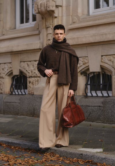 Suéter marrón de punto, pantalones de pierna ancha color crema, zapatos marrones oscuros y un gran bolso de cuero marrón, acompañado de una bufanda y un cinturón a juego.