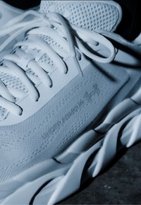 Artimos baltos sportinės avalynės vaizdas, kurio storas sukryžiuotas padas ir matomos raištelės ant tamsios paviršiaus.